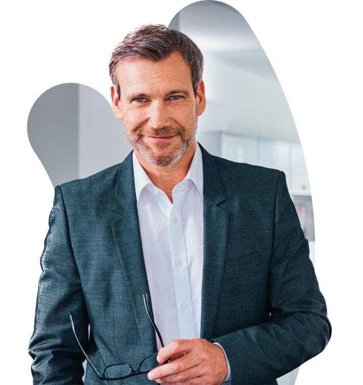 A senior living executive in a suit holding his glasses standing in front of a blurred-out office space.